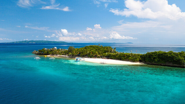 Aerial view of Boracay Island featuring a pristine white sand beach, turquoise waters, lush tropical vegetation, and boats anchored along the shore in Malay, Western Visayas, Philippines.