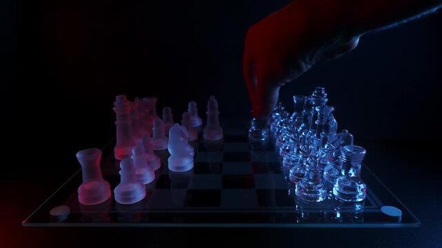 Close-up shot of a hand setting up transparent glass chess pieces on a chessboard back to their starting position.