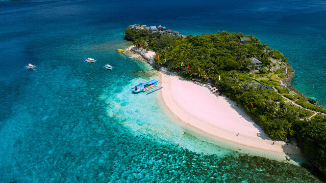 Aerial view of Boracay Island featuring a pristine white sand beach, turquoise waters, lush tropical vegetation, and traditional outrigger boats in Malay, Western Visayas, Philippines.