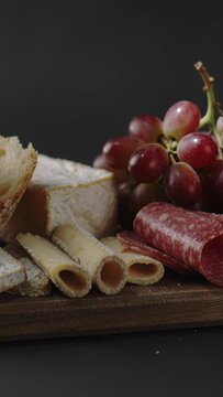 Vertical video: Camera pushing wood board into focus on table, showing brie salami crisps grapes