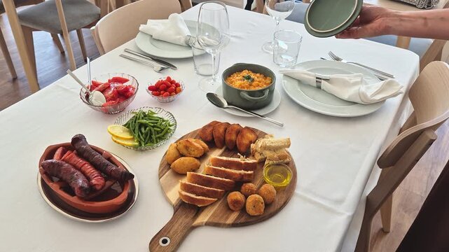 Elegant table setting for two with a traditional Portuguese lunch featuring salad, tomato, green beans, rice, chouri&ccedil;o, croquettes, cod fritters, bread and olive oil.