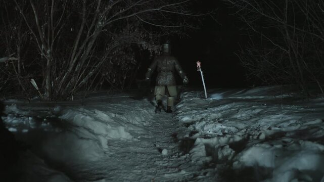 Lone armored warrior walks steadily along snow covered path at night in forest. scene features chainmail armor and medieval weaponry with bare trees silhouetted against darkness