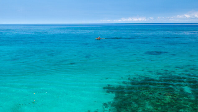 Aerial view of Boracay Island with a small boat sailing on the clear turquoise waters under a bright blue sky Malay, Western Visayas, Philippines.