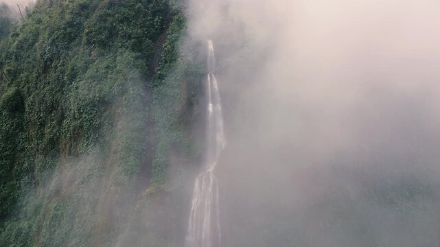 Tall Tropical Waterfall Partly Concealed by Drifting Mountain Mist