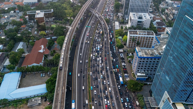 Aerial view of a busy highway in Jakarta with heavy traffic, a modern elevated train line running alongside, surrounded by urban buildings in Jakarta, Indonesia.