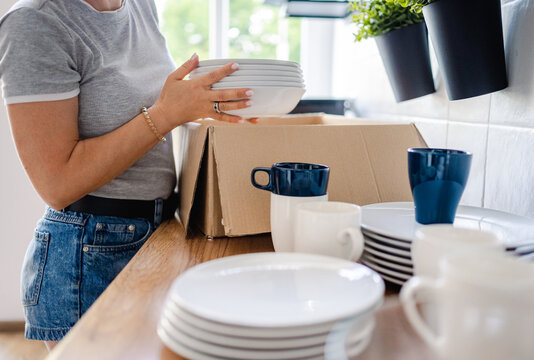 Person carefully places stack of kitchen plates into cardboard box during daytime move
