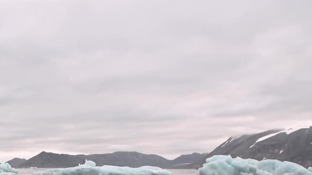 A blue iceberg floats on cold water beneath rugged mountain slopes. The composition keeps foreground detail clearly visible while the framing emphasizes scale and texture.