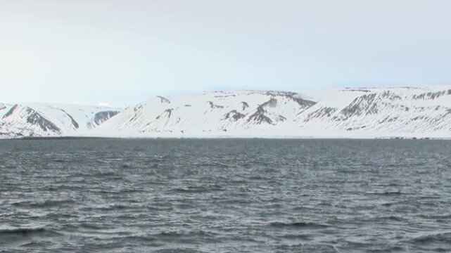 Cold Arctic Waters Glowing Beneath Wide Polar Sky Across the Far North. Snow-covered mountains remain visible beyond the cold open water and the distant polar horizon.