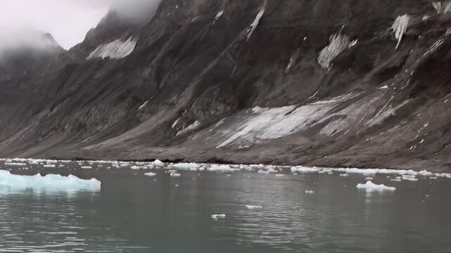 Rugged mountains rise above cold water scattered with floating ice. The frame also shows natural light and surface texture, adding visible texture and spatial context to the scene.