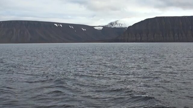 Cold Arctic Waters Moving Under Cloudy Arctic Sky in Cold Northern Air. Dark swells move across the cold water while the distant polar horizon remains clearly visible.