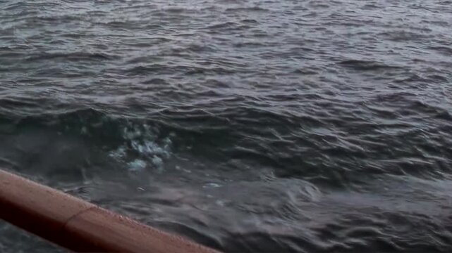Arctic Ocean Ship Navigating Grey Ocean Waters Through Remote Waters. Railing and deck elements frame the view while cold water stretches toward the distant polar horizon.