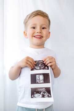 Smiling young boy holding ultrasound photos announcing baby sibling and family pregnancy excitement at home