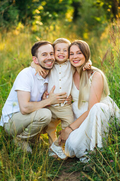 Happy family portrait of parents and young son smiling together in a sunlit summer meadow