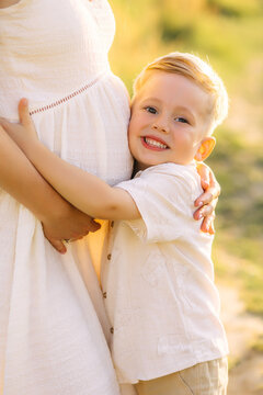 Smiling young boy hugging his pregnant mother's belly in a warm outdoor family maternity portrait