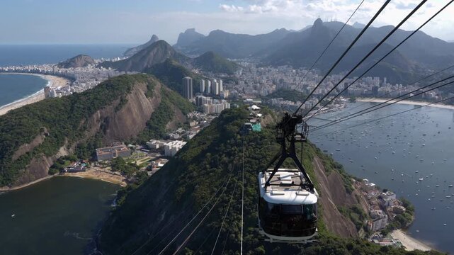 Cable car descending toward Morro da Urca with a sweeping view of Rio de Janeiro from the top of Sugarloaf Mountain on a sunny day, Brazil.