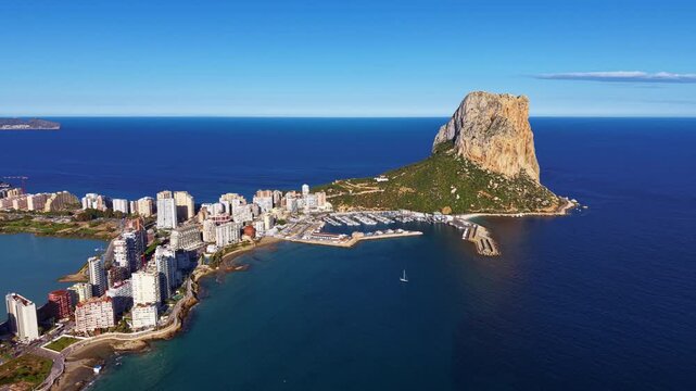Panoramic aerial view of Calpe, Spain, featuring the iconic Penon de Ifach limestone rock, marina, Mediterranean coastline, and resort buildings under blue sky