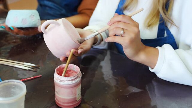 Woman applying glaze inside handmade ceramic mug with brush in pottery workshop. Pottery glazing process represents ceramic craft and handmade production