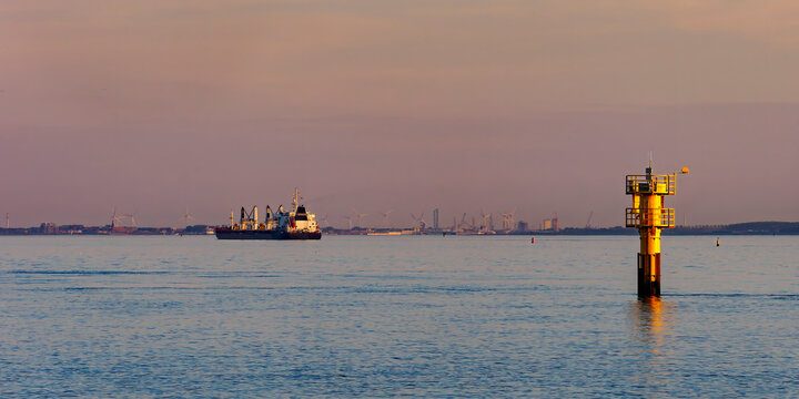 Cargo ship passing navigation buoy at sunset in Zeeland