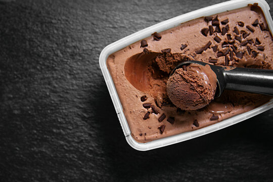 Chocolate ice cream with chocolate chips in a plastic container, photographed from above on a dark textured background.