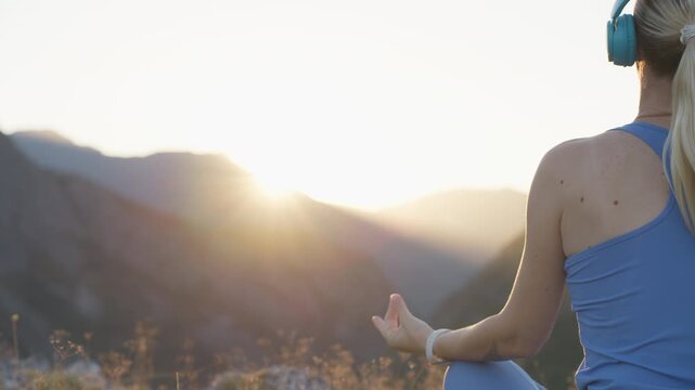 Young woman listening to music through headphones while relaxing alone in mountains, escaping busy lifestyle and finding quiet time for mindfulness, relaxation, nature, mental wellbeing