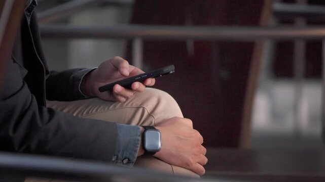 Slow motion follows hands holding a smartphone above tan trousers in Taipei, with a black jacket, denim cuff and rectangular wristwatch visible in a close seated view that keeps the face out of frame.