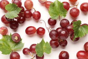 Fototapeta premium Fresh ripe grapes and green leaves on white background, flat lay