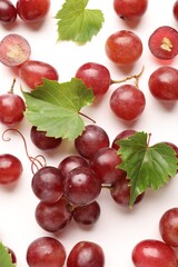 Fototapeta premium Fresh ripe grapes and green leaves on white background, flat lay