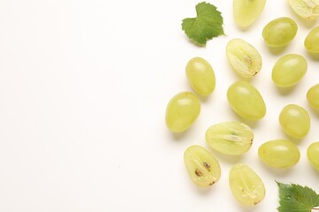 Fototapeta premium Fresh ripe grapes and green leaves on white background, flat lay. Space for text