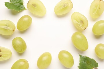 Fototapeta premium Fresh ripe grapes and green leaves on white background, flat lay. Space for text