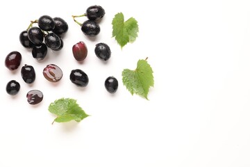 Fototapeta premium Fresh ripe grapes and green leaves on white background, flat lay. Space for text