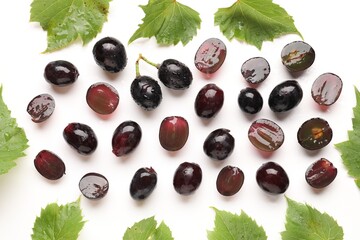 Fototapeta premium Fresh ripe grapes and green leaves on white background, flat lay