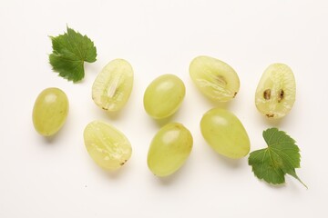 Fototapeta premium Fresh ripe grapes and green leaves on white background, flat lay