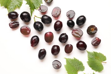 Fototapeta premium Fresh ripe grapes and green leaves on white background, flat lay
