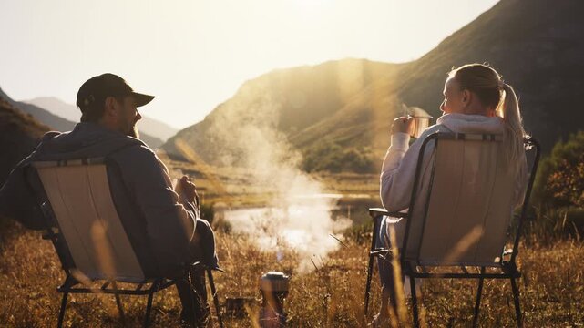 Couple enjoy digital detox in mountains, sitting together in camping chairs and watch sunset without smartphones, embracing quality time, nature, relaxation, slower lifestyle away from technology