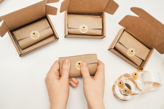 Small business owner preparing handmade orders for shipping with personalized thank you stickers