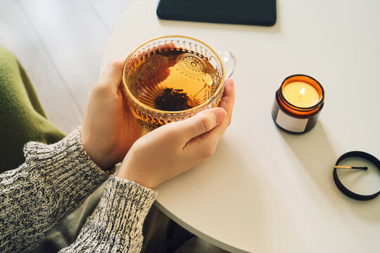 Woman taking a digital detox break from smartphone, enjoying tea and candle at home