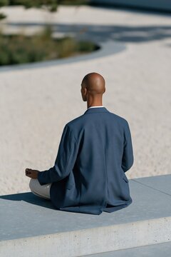 Person meditating in blue blazer seated at minimalist zen garden with raked sand for background and calm design