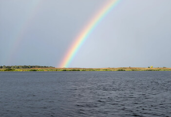 Fototapeta premium Hope and optimism concept, bright rainbow over a calm lake landscape with grassy horizon after a storm, weather phenomenon in nature and environment