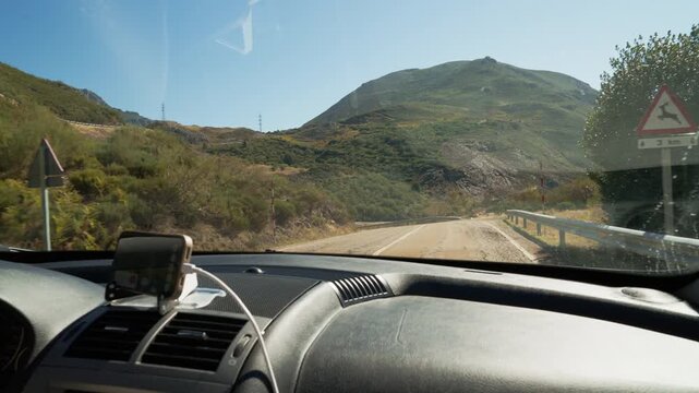 First person view of a car driving along a curvy mountain road on a sunny day with a gps navigator on the dashboard, showing the driver's perspective on a road trip adventure