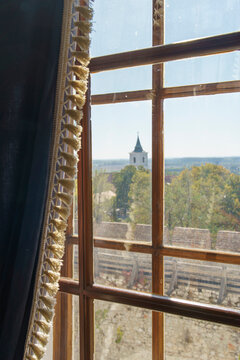 Scenic view through a wooden window frame with tasseled curtain showing a distant castle church tower and colorful autumn landscape