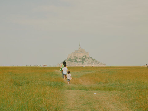 Family with children walking away across a marsh field toward Mont Saint-Michel in Normandy, France.