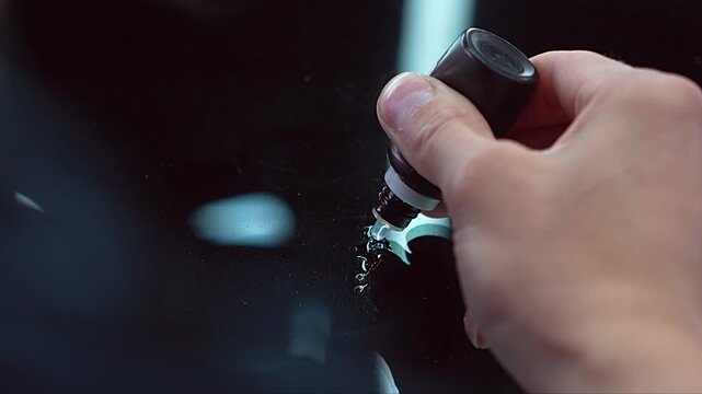 Professional mechanic fixing and restoring chipped car windshield glass close up, auto technician using special polymer resin injector tool kit to repair chip and crack damage on vehicle windscreen. 