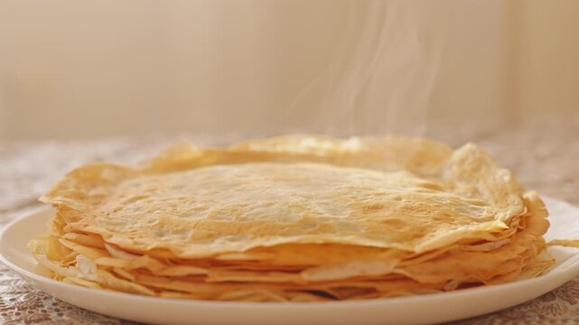 Hot steam rises from stack of fresh homemade pancakes on white plate during detailed slow motion view. Cinematic morning breakfast video footage provides warm cozy asset for design element.