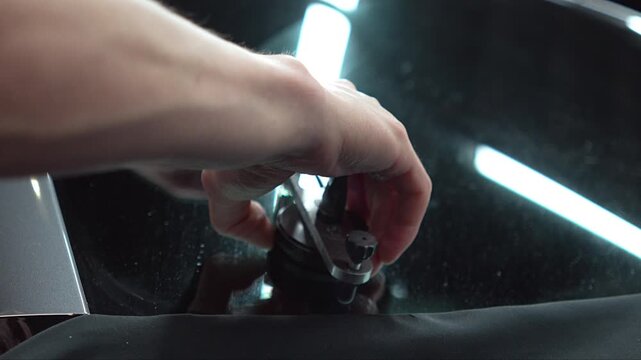 Professional mechanic fixing and restoring chipped car windshield glass close up, auto technician using special polymer resin injector tool kit to repair chip and crack damage on vehicle windscreen. 