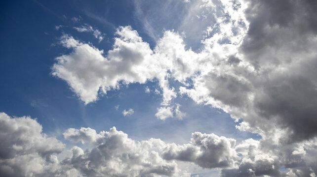 Cielo azul con nubes blancas y grises iluminadas por la luz del sol