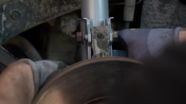 Mechanic hands in gloves installing a new silver front suspension strut shock absorber with coil spring into a car wheel well during a repair process in a workshop, close up of car maintenance. 