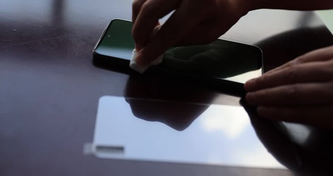 Hand carefully cleaning the screen of the smart phone before put a transparent film on a black screen of modern smartphone lying on wooden table, process of Film application of protective glass