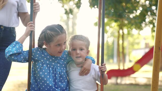two children on swing. concept of a happy childhood and loving family. girl and boy lifestyle in beautiful clothes swings on a swing on the playground, they are being filmed by their parents