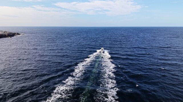 Cinematic drone footage of a white motorized fishing boat moving quickly across the ocean at dawn, traveling past the rocky shoreline of Prospect, Nova Scotia, Canada.