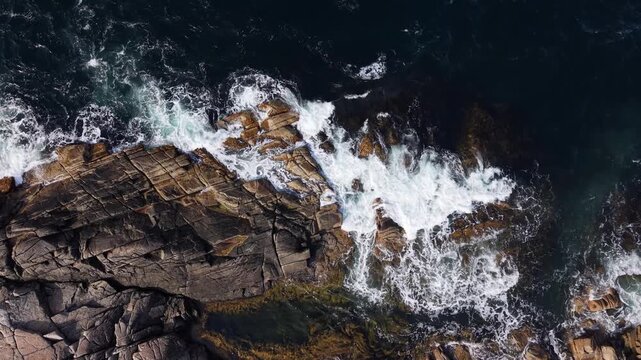 High-angle drone footage over the Atlantic coast in Prospect, Nova Scotia, featuring steep rocky formations surrounded by waves breaking along the rugged shoreline.